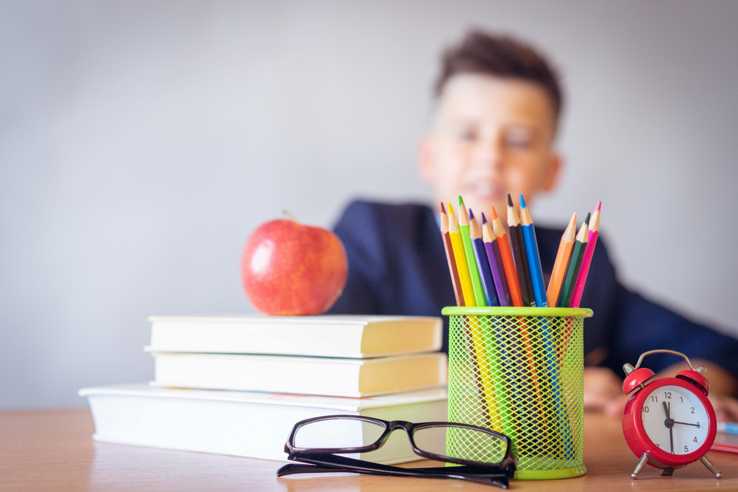 Schüler sitzt am Schreibtisch mit Brille, Stiften und Büchern